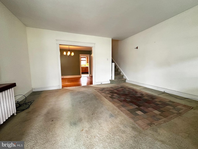 carpeted empty room with a chandelier, radiator heating unit, stairway, and baseboards