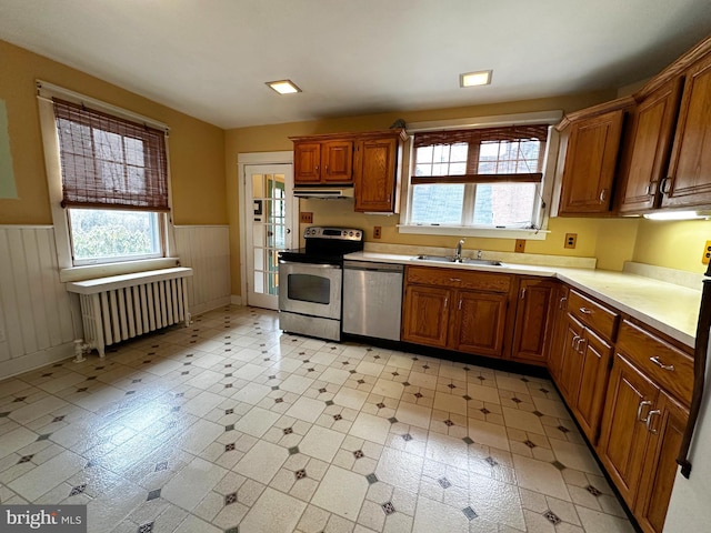 kitchen with radiator, brown cabinets, stainless steel appliances, light countertops, and under cabinet range hood