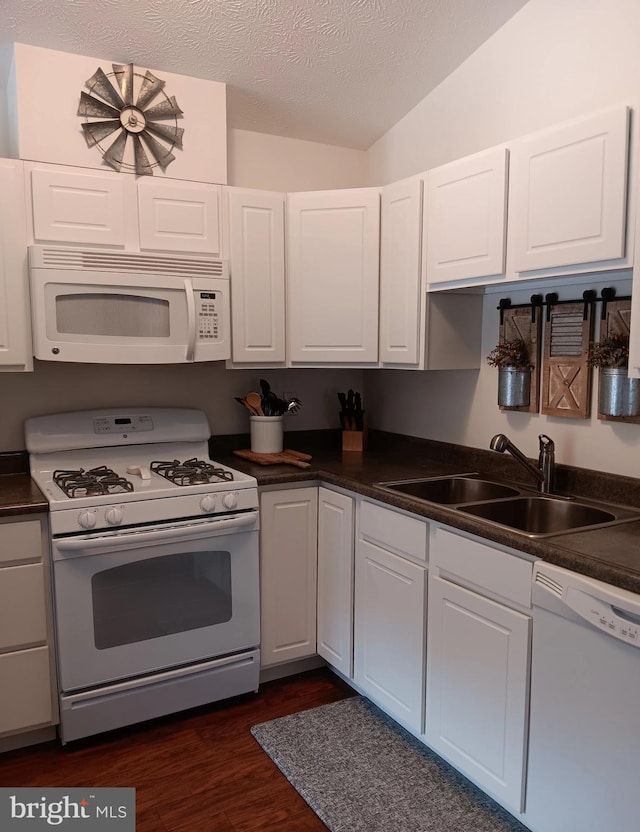 kitchen with white appliances, dark countertops, a sink, and white cabinets