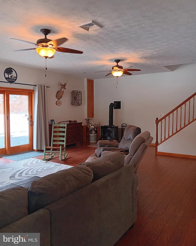 living area with a wood stove, visible vents, ceiling fan, and wood finished floors