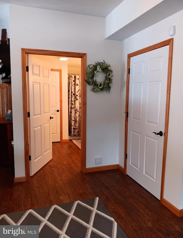 corridor featuring dark wood-type flooring and baseboards