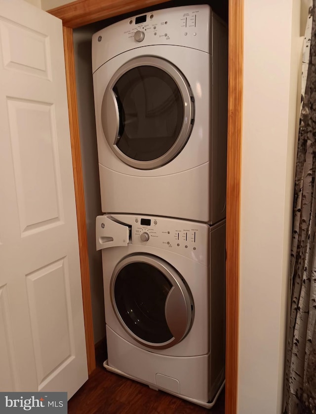 washroom with dark wood-type flooring, stacked washer / drying machine, and laundry area