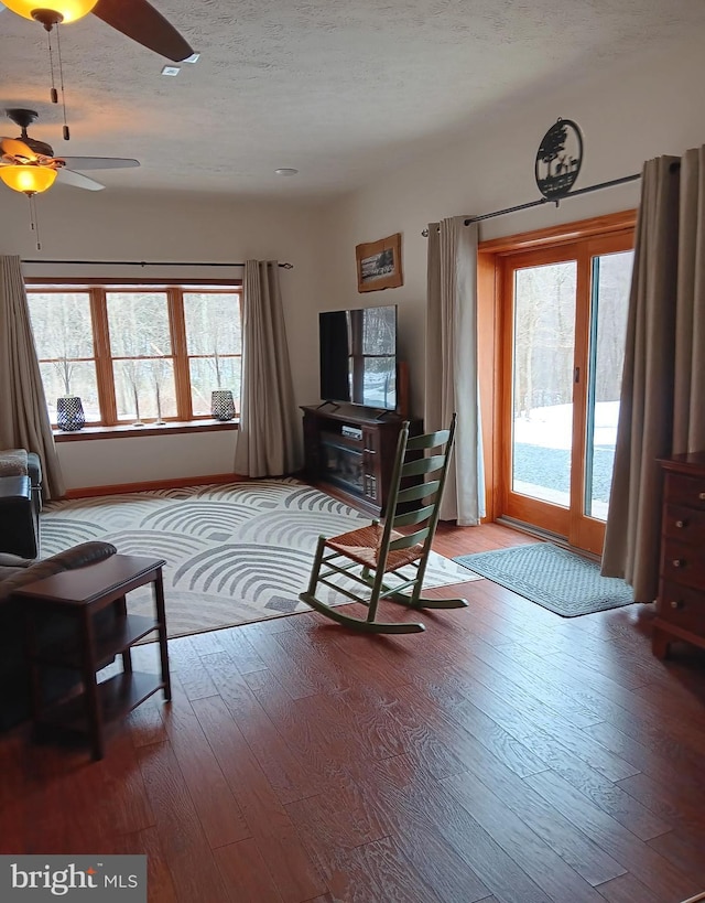 living area with a ceiling fan, light wood-type flooring, a textured ceiling, and baseboards