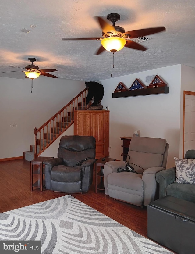 living room with a textured ceiling, ceiling fan, stairway, and wood finished floors