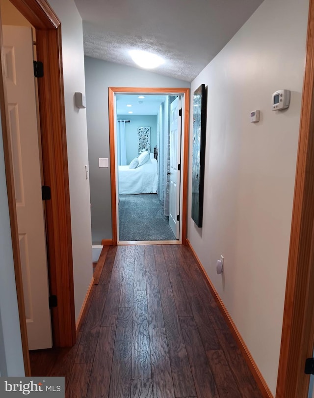 corridor with vaulted ceiling, a textured ceiling, dark wood finished floors, and baseboards