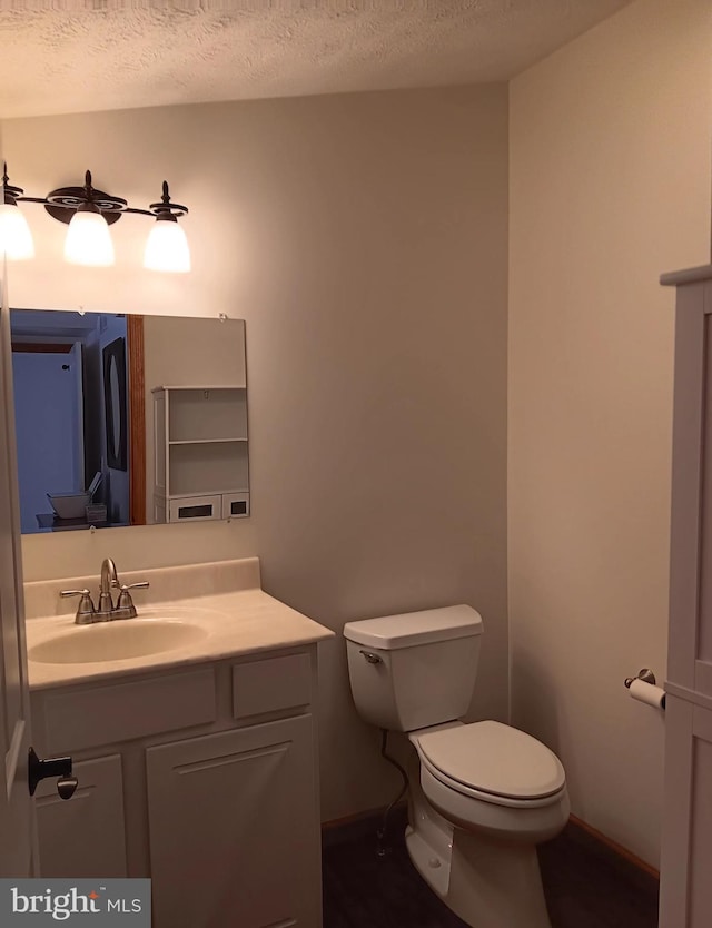 half bathroom featuring toilet, baseboards, a textured ceiling, and vanity