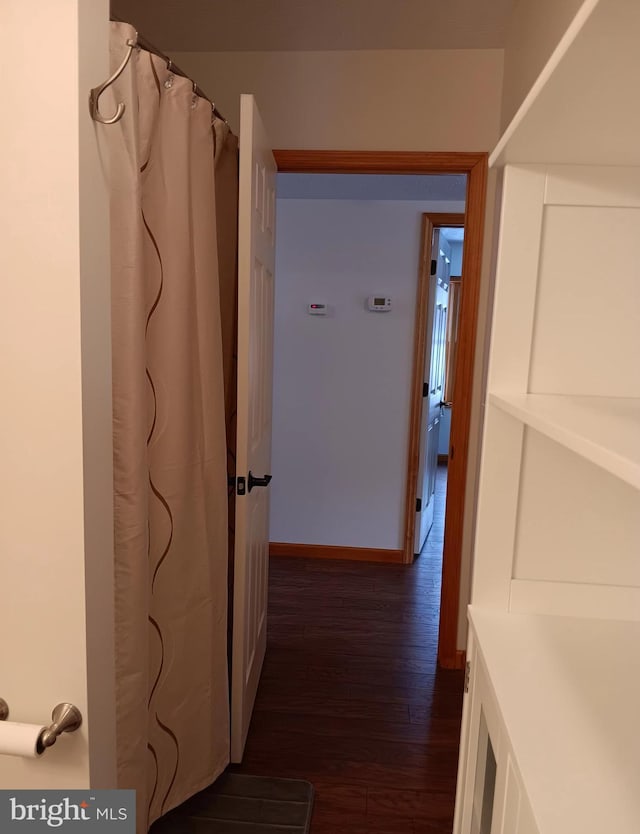 corridor with dark wood-type flooring and baseboards