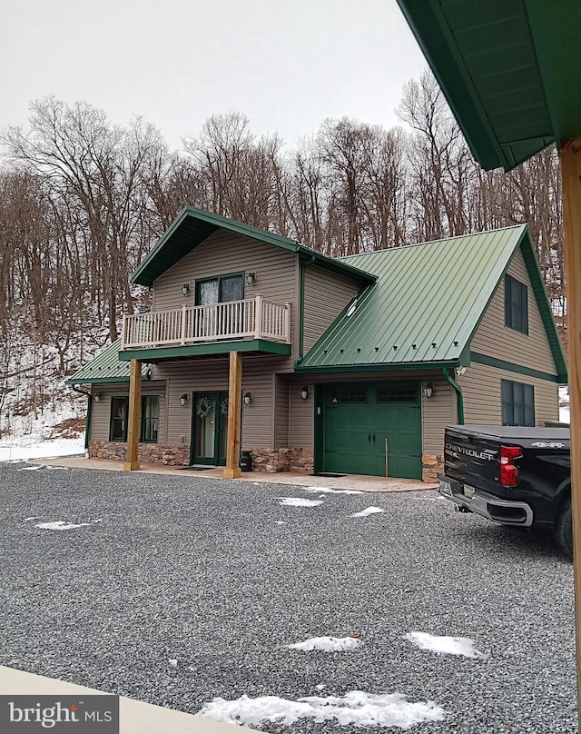 view of front of house with metal roof, stone siding, an attached garage, and a balcony