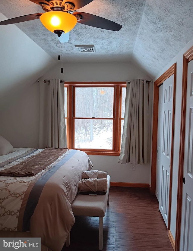 bedroom with lofted ceiling, visible vents, dark wood-style flooring, and a textured ceiling