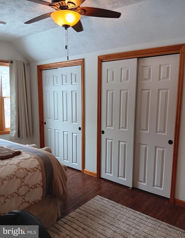 bedroom with dark wood-style floors, lofted ceiling, a textured ceiling, and two closets