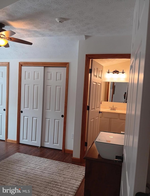 interior space featuring a textured ceiling, ceiling fan, wood finished floors, vanity, and baseboards