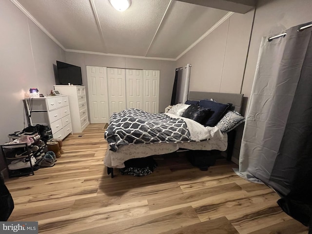 bedroom with a textured ceiling, light wood-style flooring, vaulted ceiling, ornamental molding, and a closet