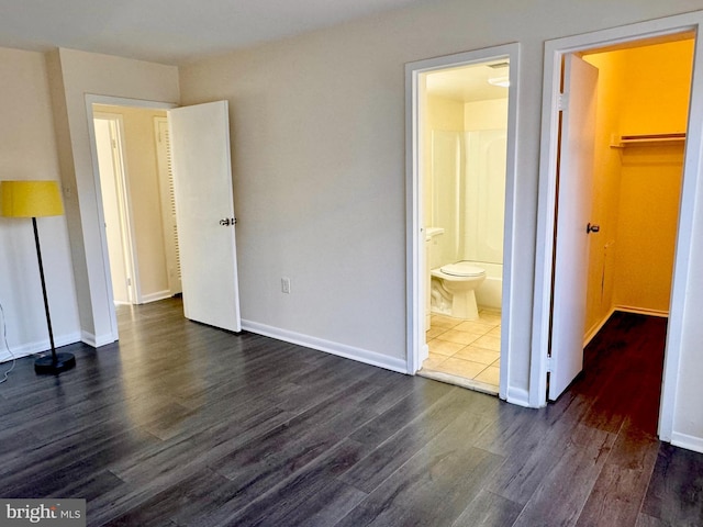 unfurnished bedroom with connected bathroom, baseboards, dark wood-style flooring, and a spacious closet