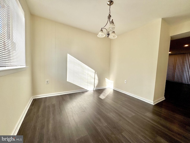 unfurnished dining area with a chandelier, baseboards, and dark wood-style flooring