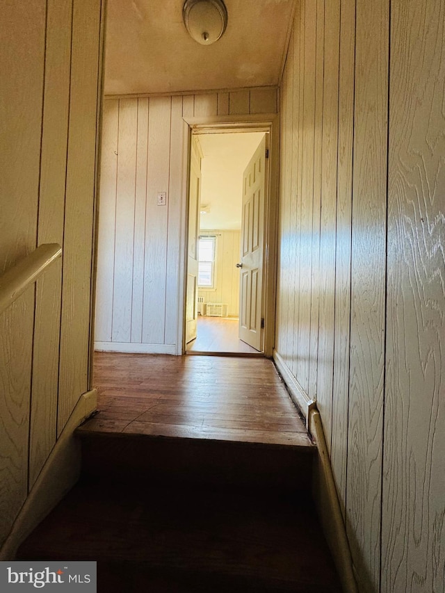 corridor with light wood-style floors, radiator heating unit, and wooden walls