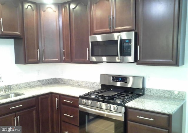 kitchen featuring dark brown cabinetry, appliances with stainless steel finishes, light stone countertops, and sink