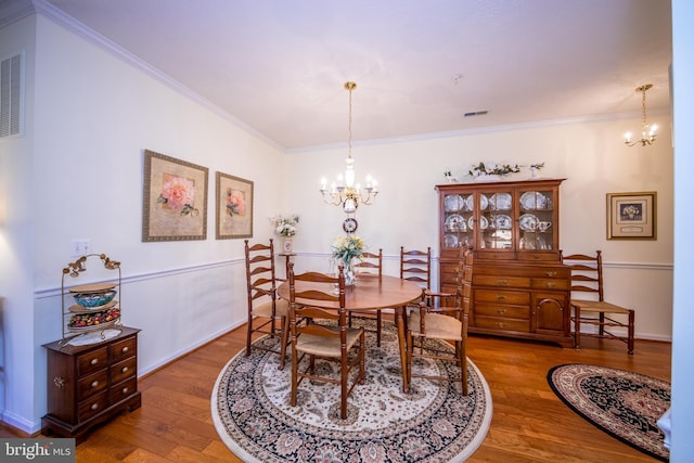 dining space with wood-type flooring, ornamental molding, and a chandelier