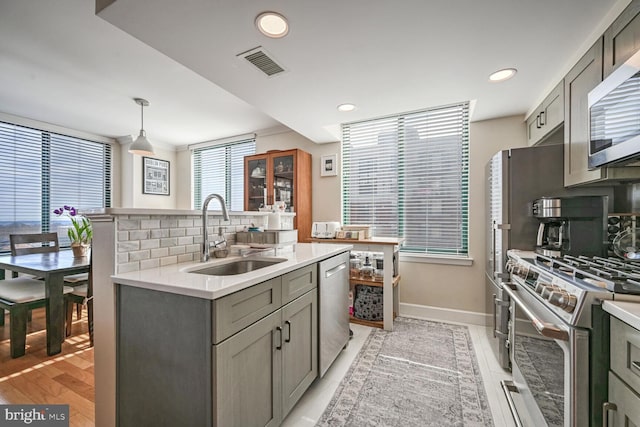 kitchen featuring pendant lighting, stainless steel appliances, gray cabinets, and sink