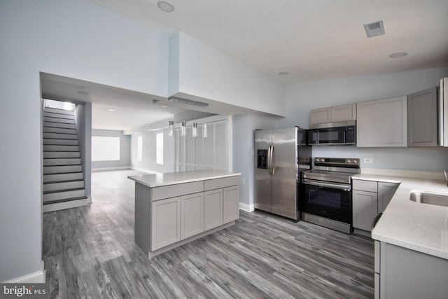 kitchen with appliances with stainless steel finishes, hardwood / wood-style floors, and gray cabinetry