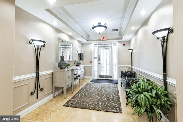 foyer featuring a raised ceiling, visible vents, a decorative wall, ornamental molding, and wainscoting