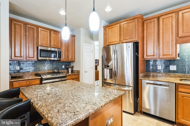 kitchen featuring appliances with stainless steel finishes, pendant lighting, brown cabinets, and light stone countertops