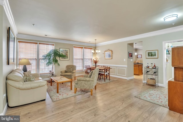 living room featuring a decorative wall, a wainscoted wall, a notable chandelier, light wood-type flooring, and crown molding