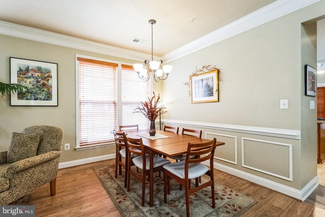 dining space with visible vents, an inviting chandelier, ornamental molding, wainscoting, and wood finished floors