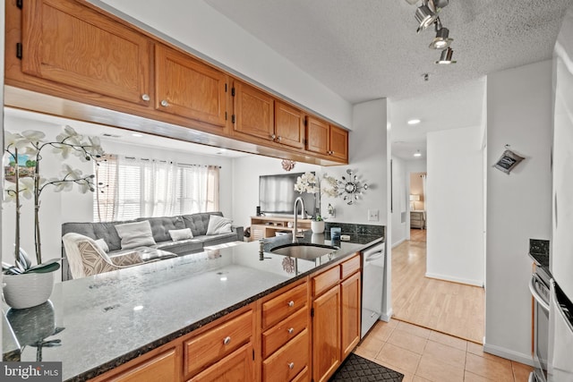 kitchen with sink, a textured ceiling, light tile patterned floors, dark stone countertops, and stainless steel dishwasher