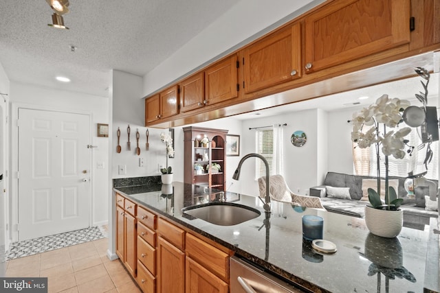 kitchen with dishwasher, sink, dark stone counters, light tile patterned floors, and a textured ceiling