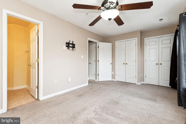 unfurnished bedroom with connected bathroom, light colored carpet, ceiling fan, and multiple closets