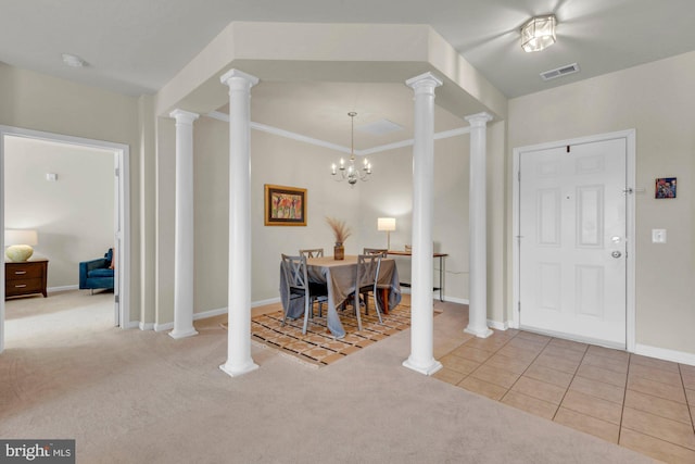 carpeted foyer entrance with a notable chandelier, ornamental molding, and decorative columns