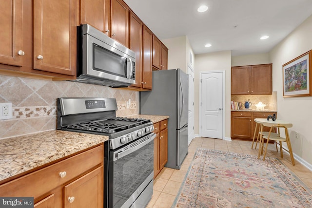 kitchen with appliances with stainless steel finishes, light tile patterned floors, light stone counters, and backsplash