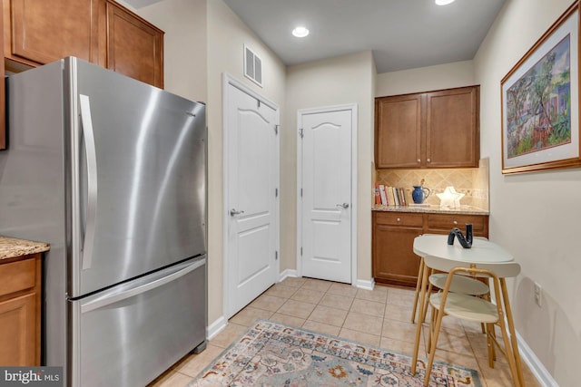 kitchen featuring light stone counters, stainless steel fridge, decorative backsplash, and light tile patterned floors