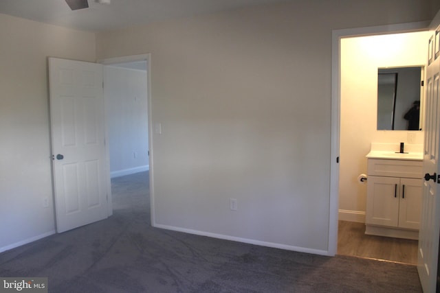 unfurnished bedroom featuring dark colored carpet, ensuite bath, a sink, and baseboards