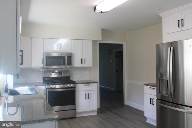 kitchen with white cabinets, dark wood finished floors, stainless steel appliances, stone counters, and backsplash