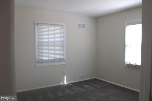 spare room with dark carpet, visible vents, and baseboards