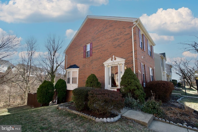 view of property exterior with fence, a lawn, and brick siding