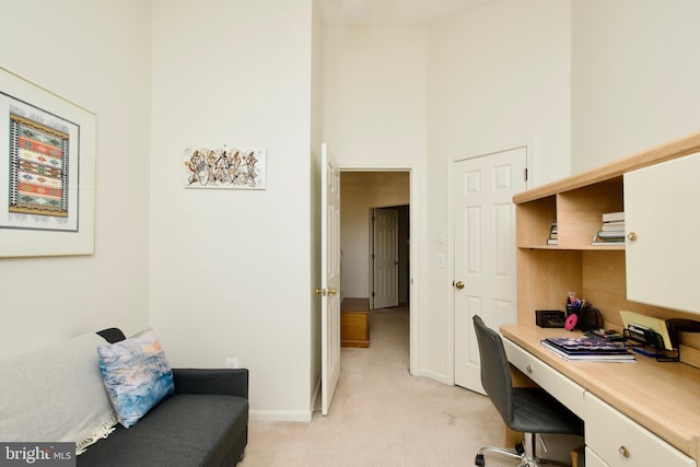 home office with a towering ceiling, baseboards, and light colored carpet