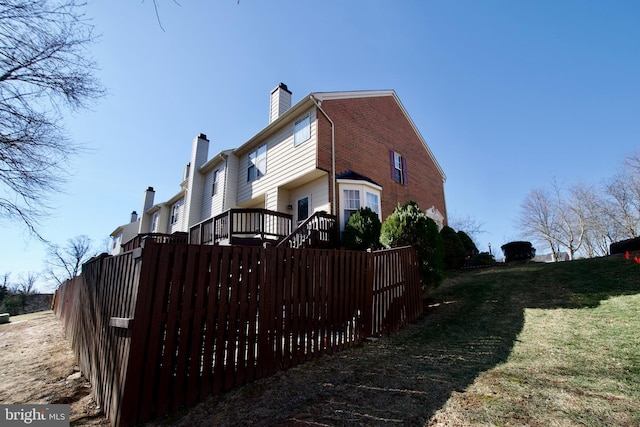 view of home's exterior with a yard, a chimney, fence, and brick siding