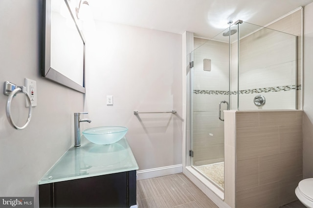 bathroom featuring a stall shower, toilet, vanity, and baseboards