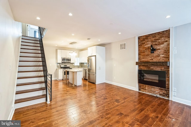 unfurnished living room with hardwood / wood-style flooring, recessed lighting, visible vents, baseboards, and stairway