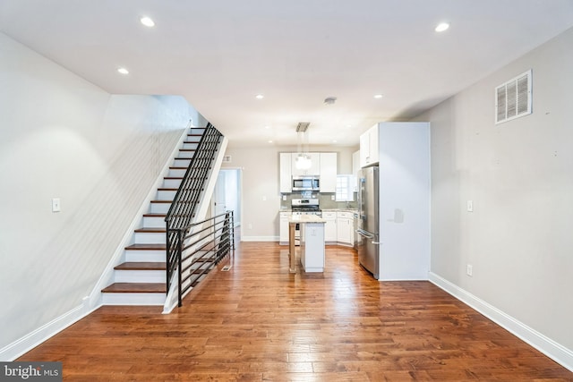 kitchen with a center island, stainless steel appliances, visible vents, white cabinets, and wood finished floors