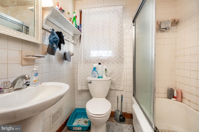 full bathroom featuring sink, toilet, combined bath / shower with glass door, and tile walls