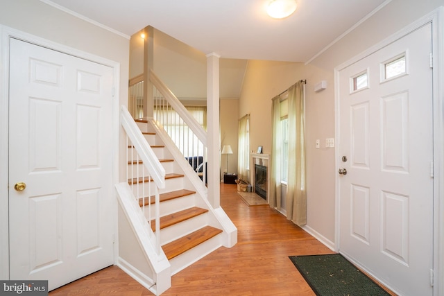 entryway with ornamental molding, stairs, light wood-style floors, a glass covered fireplace, and baseboards