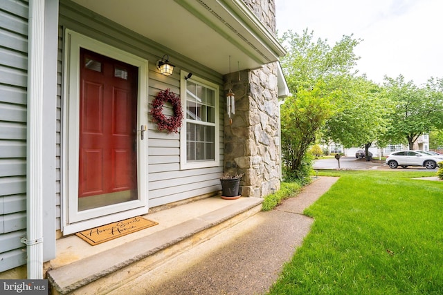 view of exterior entry with stone siding, a lawn, and a porch