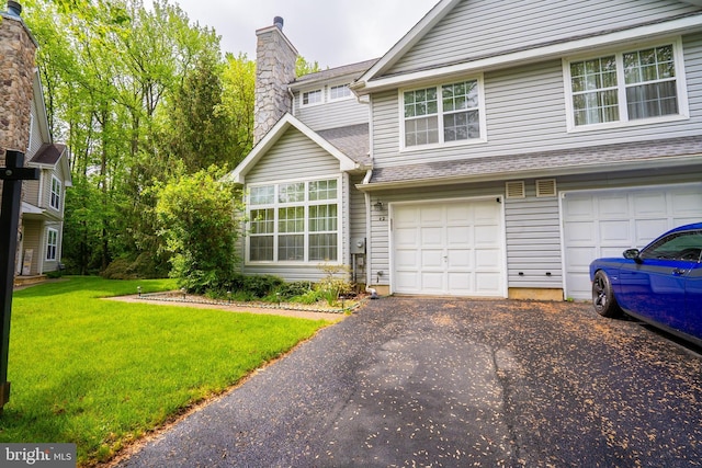 view of front facade with driveway, a front lawn, a chimney, an attached garage, and a shingled roof