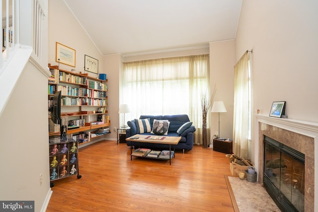 sitting room with a premium fireplace, lofted ceiling, wood finished floors, and ornamental molding