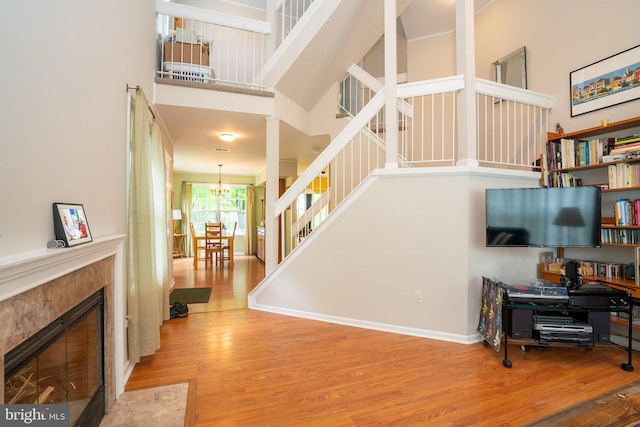 stairs with a towering ceiling, wood finished floors, a chandelier, a premium fireplace, and baseboards