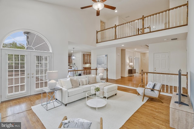 living area with visible vents, ceiling fan, a towering ceiling, wood finished floors, and french doors
