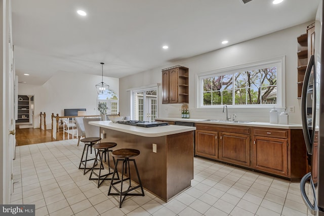 kitchen with a kitchen breakfast bar, stainless steel refrigerator, open shelves, gas cooktop, and a sink